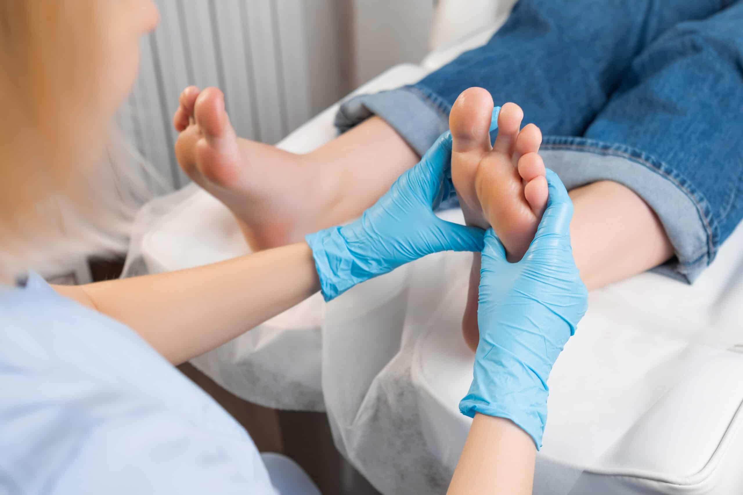 A person wearing blue gloves gently massages another person's foot at the Stanmore Wellness Clinic. The recipient, in rolled-up jeans with feet elevated, enjoys the clean, professional spa-like environment where foot health takes center stage.