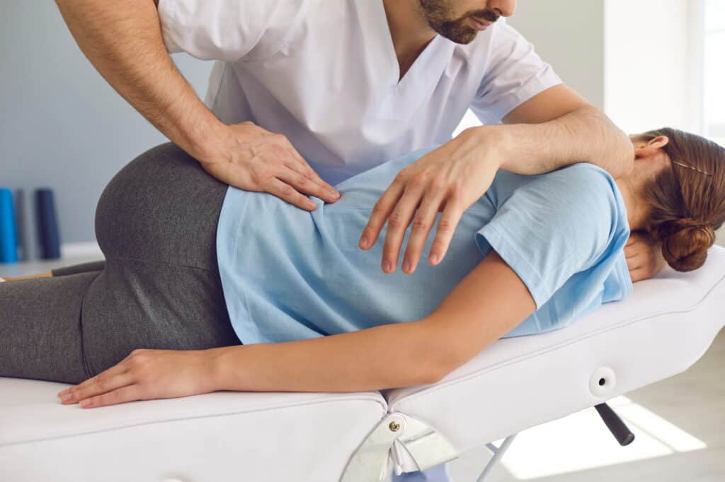 A chiropractor in a white uniform performs a lower back adjustment for pain relief as the patient lies on their side, demonstrating a commitment to holistic health.